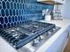 A close-up of a modern stovetop with stainless steel accents and a stylish blue tile backsplash at 1575 Trailmore Ln, Summerville, SC 29486