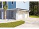 View of the two-car garage with white doors, a palm tree, and ample parking space at 1327 Wood Sorrel Dr, Moncks Corner, SC 29461