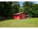 Red barn with white crossbuck doors nestled among mature trees in the backyard at 225 Baxter Ln, Walterboro, SC 29488