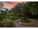 Lush backyard featuring a tiered fountain, manicured hedges, and brick pathways under a vibrant sunset sky at 5 Logan St, Charleston, SC 29401