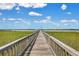 Scenic view of a wooden pier stretching out over the marsh toward the water under a bright blue sky at 2141 Sandy Point Ln, Mount Pleasant, SC 29466