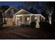 Dusk view of a brick two-story home featuring warm exterior lighting, an American flag, and cozy front porch at 5002 W Liberty Meadows Dr, Summerville, SC 29485