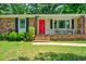 Close up of the brick home featuring a red door, front porch, and green lawn at 7 Azalea Ct, Goose Creek, SC 29445