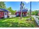 View of the backyard with green grass, a red house, a white picket fence, and trees providing shade at 8965 N Red Maple Cir, Summerville, SC 29485