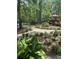 Landscaped backyard featuring a stone pathway, mature trees, lush greenery, and a wooden deck with a pink umbrella at 206 Chaussee Blvd, Summerville, SC 29483