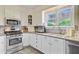 Well-lit kitchen featuring stainless steel appliances, tile backsplash, sink under a window, and white cabinets at 318 N Magnolia St, Summerville, SC 29483