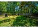 A grassy, fenced backyard featuring mature trees, patio seating, and a barbecue grill at 2016 Wild Flower Ln, Charleston, SC 29414