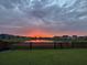 Backyard view of a pond and homes in the distance at sunset through the fenced yard at 302 Lucca Dr, Summerville, SC 29486