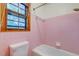 Small pink tiled bathroom featuring a toilet, tub, and window at 5322 Chantilly Ln, North Charleston, SC 29418