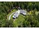 An aerial view shows a white farmhouse-style home nestled amongst lush greenery and a long circular driveway at 105 Bobcat Ln, Ravenel, SC 29470