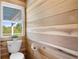 Bright bathroom featuring natural wood walls, a toilet, and a window with views of trees and the sky at 1635 Bull Creek Ln, Charleston, SC 29414