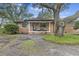 Charming brick home with a covered front porch, seating and a lovely large tree in a partially xeriscaped front yard at 1673 Mcclain St, Charleston, SC 29407