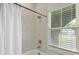 Bright bathroom with a tub and shower, white tile, window with blinds, and contrasting bronze fixtures at 868 Tripe St, Charleston, SC 29407
