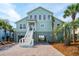Inviting two-story beach home featuring a brick driveway, lush palm trees, and an appealing coastal color palette at 313 E Arctic Ave, Folly Beach, SC 29439
