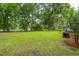 Expansive grassy backyard with mature trees and shrubbery, providing a serene outdoor setting with a covered grill area at 5195 Forest Oaks Dr, Hollywood, SC 29449
