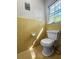 Retro bathroom with yellow tile and wallpaper, featuring a classic white toilet and natural light from the window at 411 Dogwood Circle, Summerville, SC 29485
