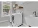 Well-lit laundry room features a modern white washer and dryer, stainless sink, shelving, and gray tile flooring at 1494 N Lakeshore Dr, Mount Pleasant, SC 29466