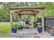 Relaxing backyard patio area with a pavilion, comfortable seating, fireplace, and grilling station surrounded by trees at 6190 Button Bush Dr, Ravenel, SC 29470