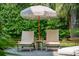 Two sun loungers shaded by an umbrella create a peaceful poolside seating area surrounded by greenery at 924 Mciver St, Mount Pleasant, SC 29464