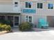 Exterior shot of Water's Edge Cafe with a blue Adirondack chair, lush greenery, and signage at 491 Sea Cloud Cir, Edisto Island, SC 29438