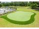 Aerial view of a well-manicured putting green next to a pond, with lounge chairs and umbrellas nearby for relaxation at 3010 Grinnell St, Johns Island, SC 29455