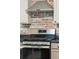 A gas range and exhaust fan sit against a brick wall in a kitchen with gray cabinets and black countertops at 108 Plume Poppy Ln, Ladson, SC 29456
