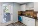 Cozy kitchen features tile backsplash, black countertop, modern dishwasher, and a door to an outdoor grill area at 1919 Marsh Oak Ln, Seabrook Island, SC 29455