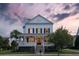 Elegant two-story home with a welcoming front porch, dark shutters, and manicured landscaping at twilight at 2489 Daniel Island Dr, Daniel Island, SC 29492