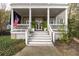 Welcoming front porch featuring white columns, stairs, and railings complemented by lush greenery and an American flag at 74 Hospitality St, Mount Pleasant, SC 29464
