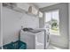 Well-lit laundry room with white front load washer and dryer, overhead storage shelf, and large window at 7035 Pumpkinseed Dr, Johns Island, SC 29455