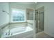 Bathroom with a large, tiled walk-in shower and a soaking tub beneath a bright window at 9710 Table Mountain Ln, Ladson, SC 29456