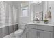 Bright bathroom with a gray vanity, toilet, a window and a bathtub with a striped shower curtain at 1439 Rivers Cotton Rd, Charleston, SC 29412