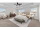 A staged main bedroom with a ceiling fan, tray ceiling, bench, carpet, and many windows at 213 Crossandra Ave, Summerville, SC 29483