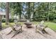 A backyard gravel area with a metal fire pit and wooden Adirondack chairs surrounded by trees at 7021 Schooner St, Charleston, SC 29492
