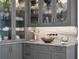 Sophisticated bar area featuring gray cabinetry, a copper sink, marble countertops, and glass-front cabinets with glassware display at 79 Trailing Vine Way, Kiawah Island, SC 29455