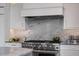 Stainless steel kitchen range with marble backsplash, white cabinetry, and stainless steel hood at 79 Trailing Vine Way, Kiawah Island, SC 29455