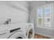Bright laundry room features a white washer and dryer, shelving, and a window with plantation shutters at 1530 Willtown St, Daniel Island, SC 29492