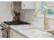 Close-up of a kitchen sink with gold faucet, stainless steel stove, white tile backsplash, and white marble countertop at 6 Sayle Rd, Charleston, SC 29407