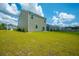 View of the backyard featuring a grassy lawn and the rear of the home, complemented by a blue sky with fluffy clouds at 1032 Peridote Way, Ladson, SC 29456