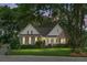 Evening view of charming brick home featuring a well-manicured lawn, and mature trees, creating an inviting curb appeal at 652 Spinner Cir, Mount Pleasant, SC 29464