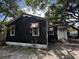Modest single-story home featuring a black exterior, brick foundation, awning accents and mature trees at 2334 Kent Ave, North Charleston, SC 29405