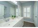 Bathroom featuring double sinks, white cabinetry, neutral tile, and a window with shutter at 2997 Sturbridge Rd, Mount Pleasant, SC 29466