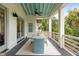 This covered porch features dining for six, white railings, a ceiling fan, and gorgeous wooded views at 55 Seagrass Ln, Isle of Palms, SC 29451