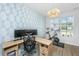 Well-lit home office with patterned wallpaper, a wooden desk, and exercise equipment by the window at 6976 Pumpkinseed Dr, Johns Island, SC 29455