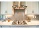 Well-lit kitchen featuring stainless steel range hood, gas cooktop, gray tile backsplash, and ample quartz countertop space at 713 Breakers Reef Ln, Huger, SC 29450