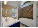 Elegant bathroom featuring double sinks, stone accent wall, and a luxurious soaking tub under a skylight at 2021 Lakeshore Dr, Charleston, SC 29412