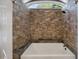 Close-up of the bathtub with unique stone-tiled walls and an arched window above at 2021 Lakeshore Dr, Charleston, SC 29412