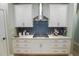 A modern kitchen features white cabinets, gold hardware, stainless steel vent hood, and blue backsplash at 4407 Palm Shadow Dr, Summerville, SC 29485