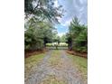 Gated driveway entrance with a pea gravel drive lined with mature trees and lush greenery at 8272 Palmetto Rd, Edisto Island, SC 29438