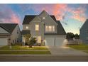 Two-story house with lights on, beige siding, a two-car garage, and landscaped front yard at 149 Cypress Preserve Blvd, Moncks Corner, SC 29461